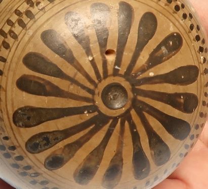 Detail of the filling ornament: a rosette of black petals radiating from an incised centre, set against the pale clay beside the wing.